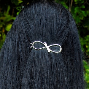 May include: A woman with long, black hair wearing a silver infinity hair clip.