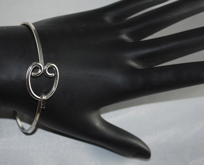 May include: A silver bangle bracelet with a heart-shaped charm. The charm is made of two interlocking circles.