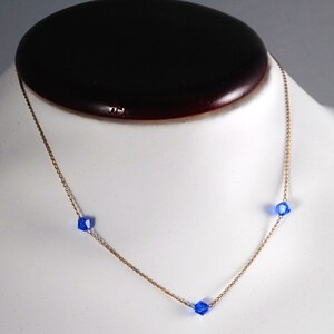 May include: A delicate gold chain necklace with three small, faceted, blue crystal beads.
