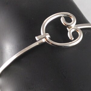 May include: A silver bangle bracelet featuring a distinctive, open, circular design. The bracelet is crafted from thin metal and has a simple, elegant appearance.