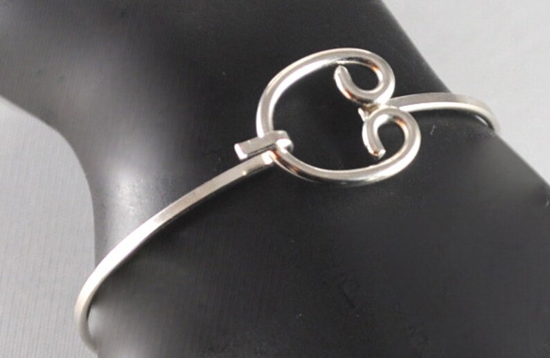 May include: A silver bangle bracelet featuring a distinctive, open, circular design. The bracelet is crafted from thin metal and has a simple, elegant appearance.