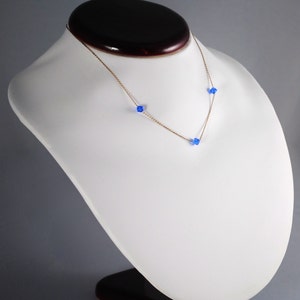 May include: A gold chain necklace with three small blue crystal beads.