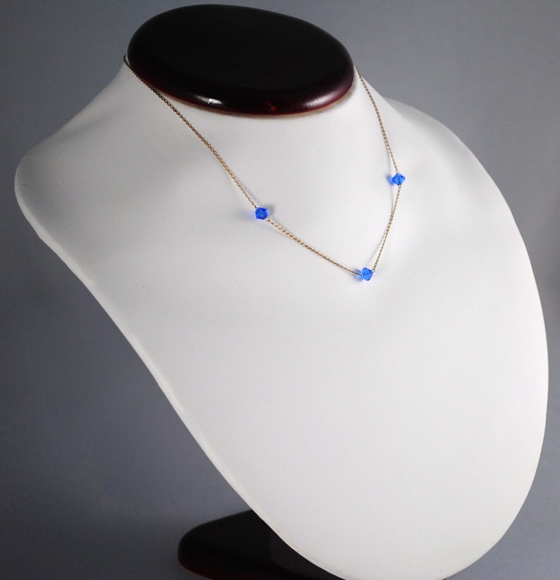 May include: A gold chain necklace with three small blue crystal beads.