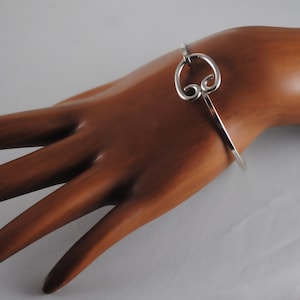 May include: A silver bangle bracelet with a decorative swirl design. The bracelet is open and has a simple clasp.