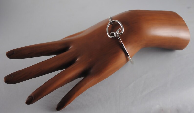 May include: A silver bangle bracelet with a decorative swirl design. The bracelet is open and has a simple clasp.