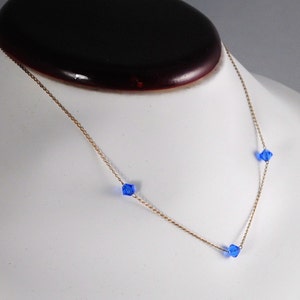 May include: A gold chain necklace with three blue crystal beads.
