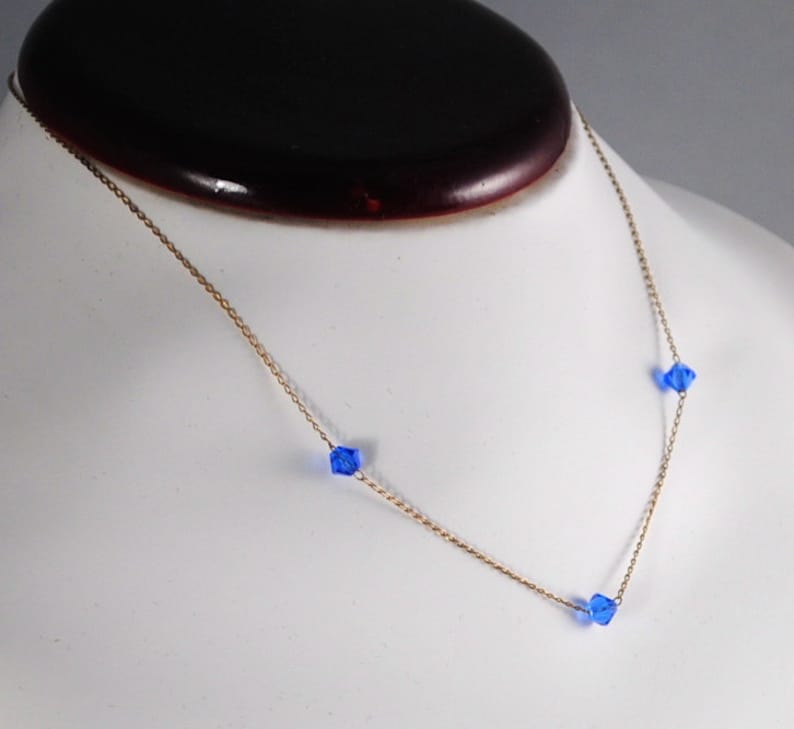 May include: A gold chain necklace with three blue crystal beads.