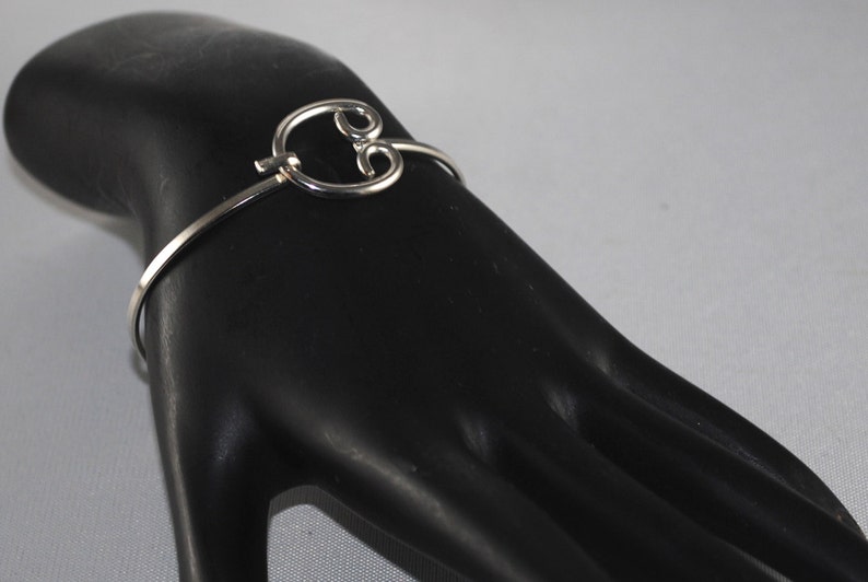 May include: A silver bangle bracelet with a decorative, open circle design. The circle is made of two overlapping loops.