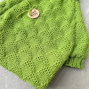 May include: A bright green knitted sweater with a turtleneck and a hand-made tag. The sweater has a unique stitch pattern.
