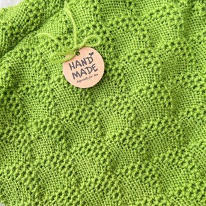 May include: A green knitted blanket with a brown tag that says "HAND MADE Especially for you".