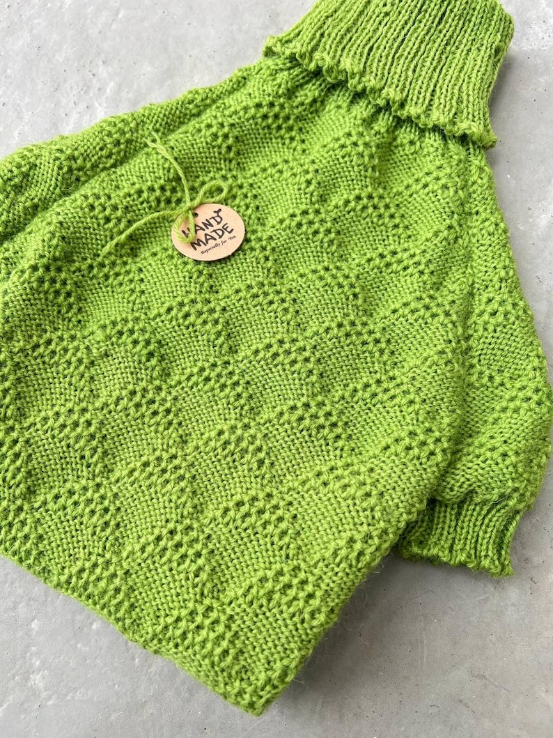 May include: A bright green knitted sweater with a turtleneck and a hand-made tag. The sweater has a unique stitch pattern.