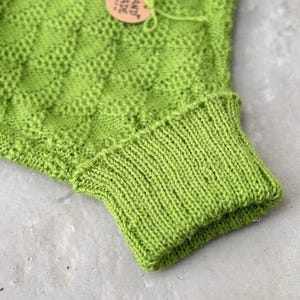May include: A bright green knitted cowl neck sweater with a hand-made tag attached. The sweater is made with a textured stitch pattern.