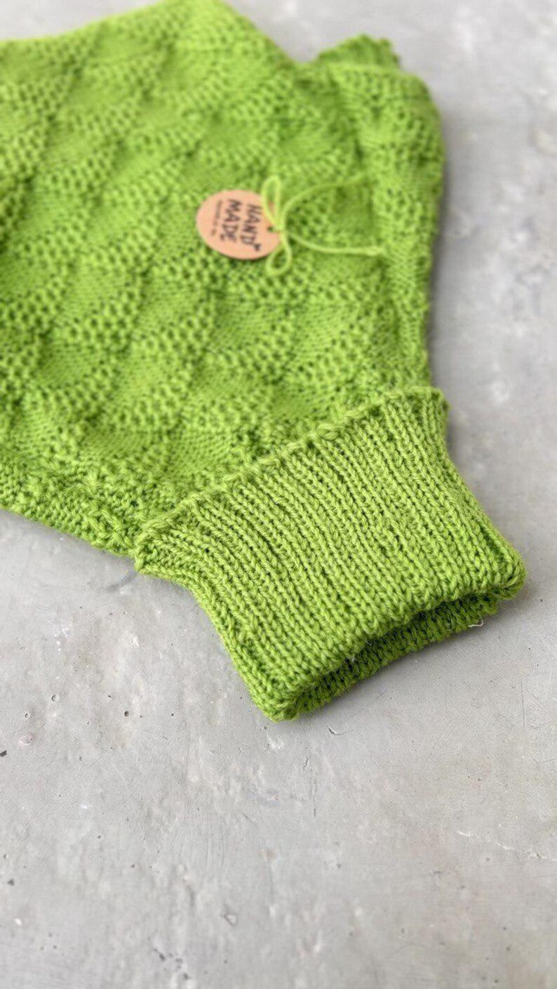 May include: A bright green knitted cowl neck sweater with a hand-made tag attached. The sweater is made with a textured stitch pattern.
