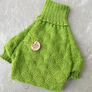 May include: A bright green knitted turtleneck sweater with a hand-made tag. The sweater has a textured pattern and is made with a soft yarn.