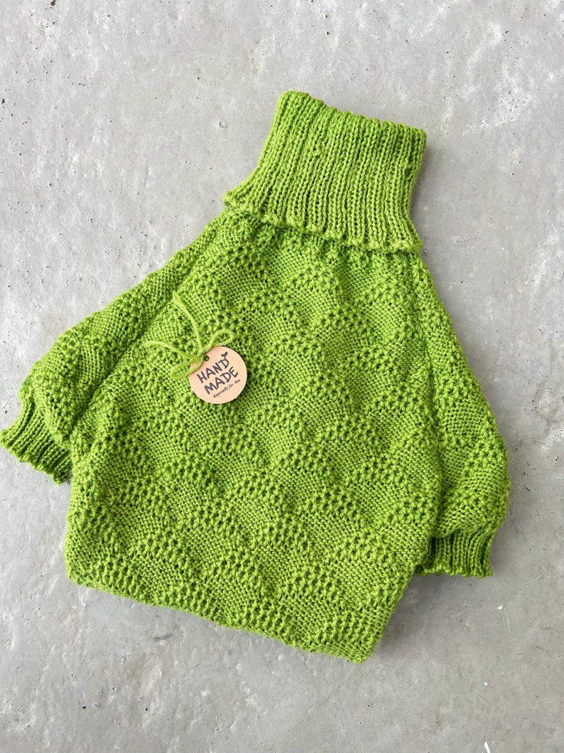 May include: A bright green knitted turtleneck sweater with a hand-made tag. The sweater has a textured pattern and is made with a soft yarn.