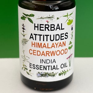 May include: A small brown glass bottle with a white cap, labeled "HERBAL ATTITUDES HIMALAYAN CEDARWOOD INDIA ESSENTIAL OIL". The label features a variety of colorful flowers and herbs.