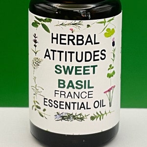 May include: A small brown glass bottle with a white cap, labeled "HERBAL ATTITUDES SWEET BASIL FRANCE ESSENTIAL OIL". The label features a floral design.