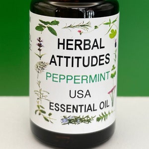 May include: A small brown glass bottle with a white cap, labeled "HERBAL ATTITUDES PEPPERMINT USA ESSENTIAL OIL". The label features a variety of green herbs and flowers.