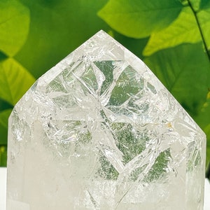 May include: A clear quartz crystal point with a unique, intricate pattern of internal fractures. The crystal is shaped like a pyramid and has a smooth, polished surface.