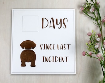 May include: White sign with brown text and a brown silhouette of a dog's rear end. The text reads "Days since last incident".