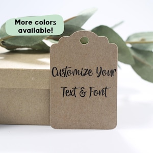 May include: A brown paper tag with a decorative top edge and a hole for hanging. The tag features the text "Customize Your Text & Font" in black. A green rectangle with the text "More colours available!" is in the upper left corner.