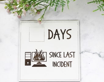 May include: White wooden sign with black text that reads "Days since last incident". The sign has a blank space for a number and a graphic of a computer on fire.