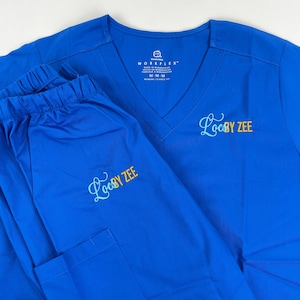 May include: A royal blue scrub top and matching pants with the text "Locs by Zee" embroidered in turquoise and gold lettering.