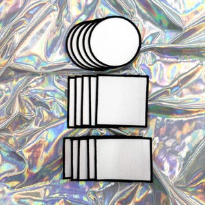 Op de afbeelding: Een verzameling witte, ronde en rechthoekige patches met zwarte randen. De patches zijn in nette rijen en kolommen gerangschikt, tegen een glinsterende, iriserende achtergrond.