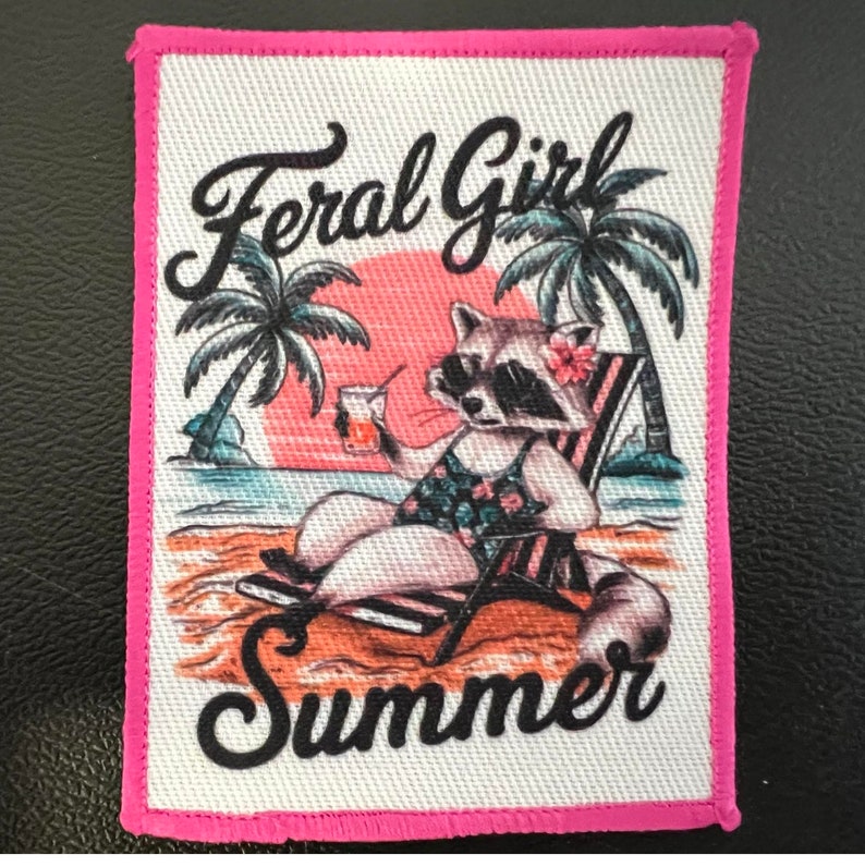 K&ouml;nnte beinhalten: Ein rechteckiger bestickter Aufn&auml;her mit pinkem Rand zeigt einen Waschb&auml;ren mit Sonnenbrille und gebl&uuml;mtem Badeanzug, der mit einem Getr&auml;nk in einem Strandstuhl sitzt. Der Hintergrund zeigt einen Strand, Palmen und den Schriftzug Feral Girl Summer.