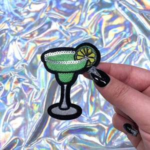 May include: Green margarita glass with a lime wedge, embroidered with sequins. The glass is on a white background.