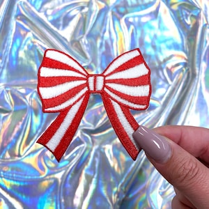 May include: Red and white striped fabric bow with a white center. The bow is embroidered and has a shiny finish.