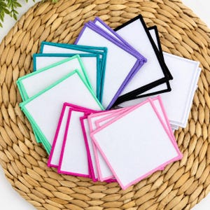 May include: A collection of square fabric patches with white centers and vibrant stitched borders in shades of purple, black, teal, mint green, magenta, and pink, arranged in a fanned-out overlapping pattern to display the various edge colors.