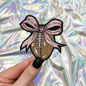 May include: A brown and white football with a pink ribbon tied around it. The ribbon is tied in a bow.
