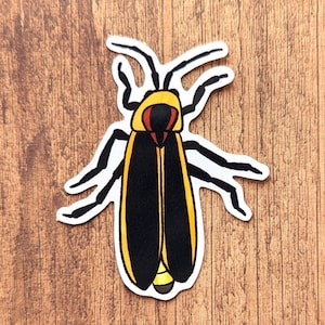 May include: A yellow and black firefly sticker with red eyes. The firefly is on a wood background.