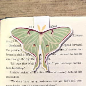 May include: A white bookmark with a green and brown luna moth illustration. The bookmark has the words "THE ( BOOKS" at the top and "Rintaro" at the bottom.