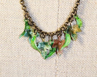 May include: A bronze-toned necklace featuring a series of leaf pendants in shades of green and bronze. The leaves vary in shape and size, with detailed veining. The chain is a matching bronze color, creating a cohesive, nature-inspired accessory.