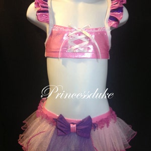 May include: Pink and purple layered tulle skirt with a large purple bow. The skirt is paired with a pink and white crop top with a lace-up front and purple ruffle straps.