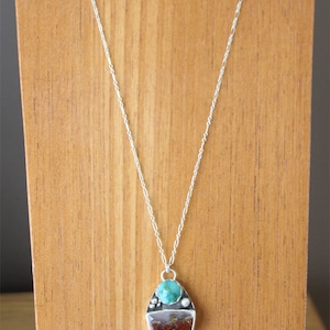 Könnte beinhalten: Eine silberne Kettenkette mit einem Anhänger aus einem Türkis-Stein, einem geschichteten Achat-Stein und einem weißen Achat-Tropfen. Die Kette wird auf einem Holzständer präsentiert.