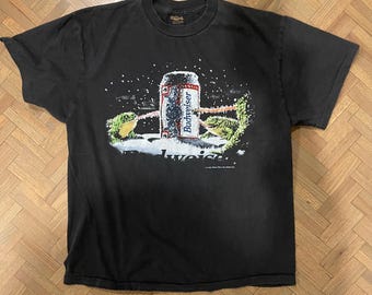 May include: Black t-shirt featuring a graphic of a Budweiser beer can in a snowy scene. The can is red, white, and blue, with the Budweiser logo. The shirt has a crew neck and short sleeves.