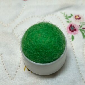 May include: A green felt pincushion in a white plastic container.
