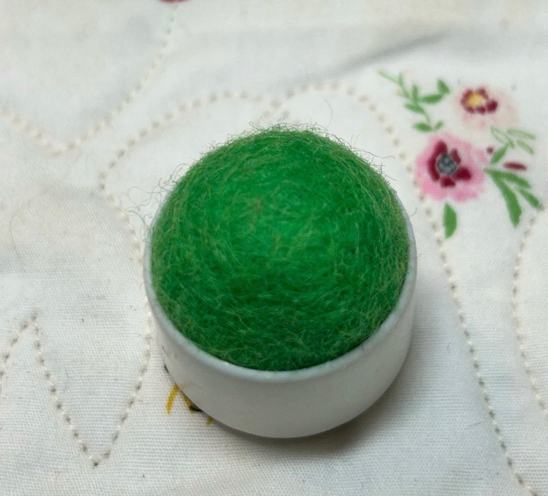 May include: A green felt pincushion in a white plastic container.