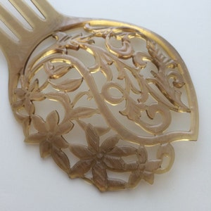 May include: A light brown hair comb with a decorative floral design. The comb features a series of tines and a detailed, openwork pattern of flowers and leaves. The comb is made of a translucent material.