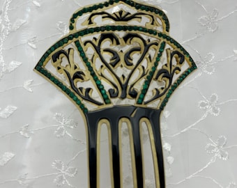 May include: An ornate black and gold hair comb with a fan-shaped design. The comb features intricate cut-out patterns, green jewel accents, and a classic three-prong base. A decorative hair accessory.