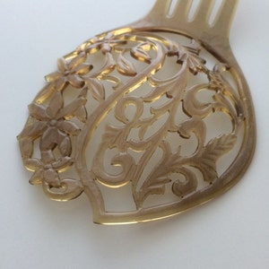 May include: A light brown hair comb with a decorative floral design. The comb features a detailed, openwork pattern of flowers and leaves. The tines of the comb are visible at the top.