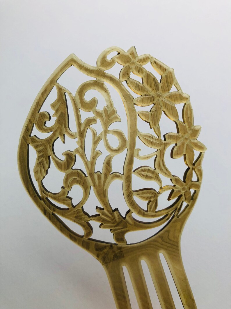 May include: A light brown hair comb with an intricate floral and leaf design. The comb features a decorative top with carved flowers and swirling patterns. The tines of the comb are visible at the bottom.