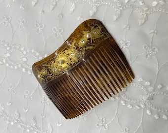 May include: A vintage tortoiseshell hair comb with ornate gold filigree and faux pearl and rhinestone accents. The comb has a curved shape and fine teeth, perfect for styling hair. The decorative elements add a touch of elegance.