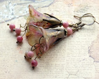 May include: A pair of pink and gold floral earrings with pink gemstone beads hanging from the bottom. The earrings are made of glass and metal.