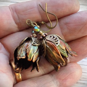 Pode incluir: Um par de brincos com design de flores. As flores s&atilde;o feitas de metal e t&ecirc;m um acabamento cobre e verde. Os brincos est&atilde;o pendurados em um gancho de lat&atilde;o.