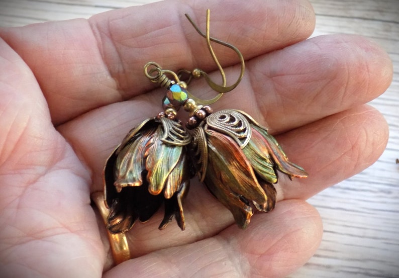 Pode incluir: Um par de brincos com design de flores. As flores s&atilde;o feitas de metal e t&ecirc;m um acabamento cobre e verde. Os brincos est&atilde;o pendurados em um gancho de lat&atilde;o.