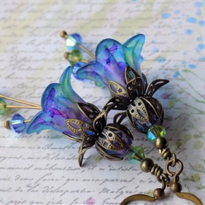 May include: A pair of blue and purple flower earrings with bronze filigree accents and crystal beads. The earrings are dangling and have a vintage style.